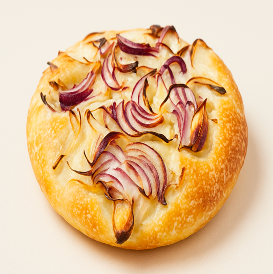 Round focaccia loaf with caramelized onions on a light beige background