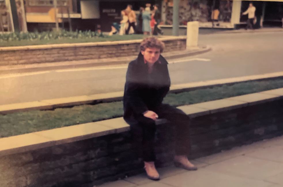 Gio sitting on a ledge in an urban setting with people and buildings in the background
