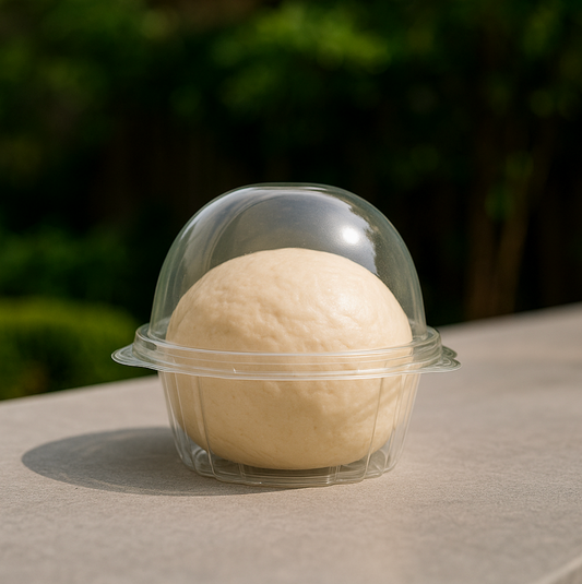 Round ball of dough in a clear plastic container on a neutral background
