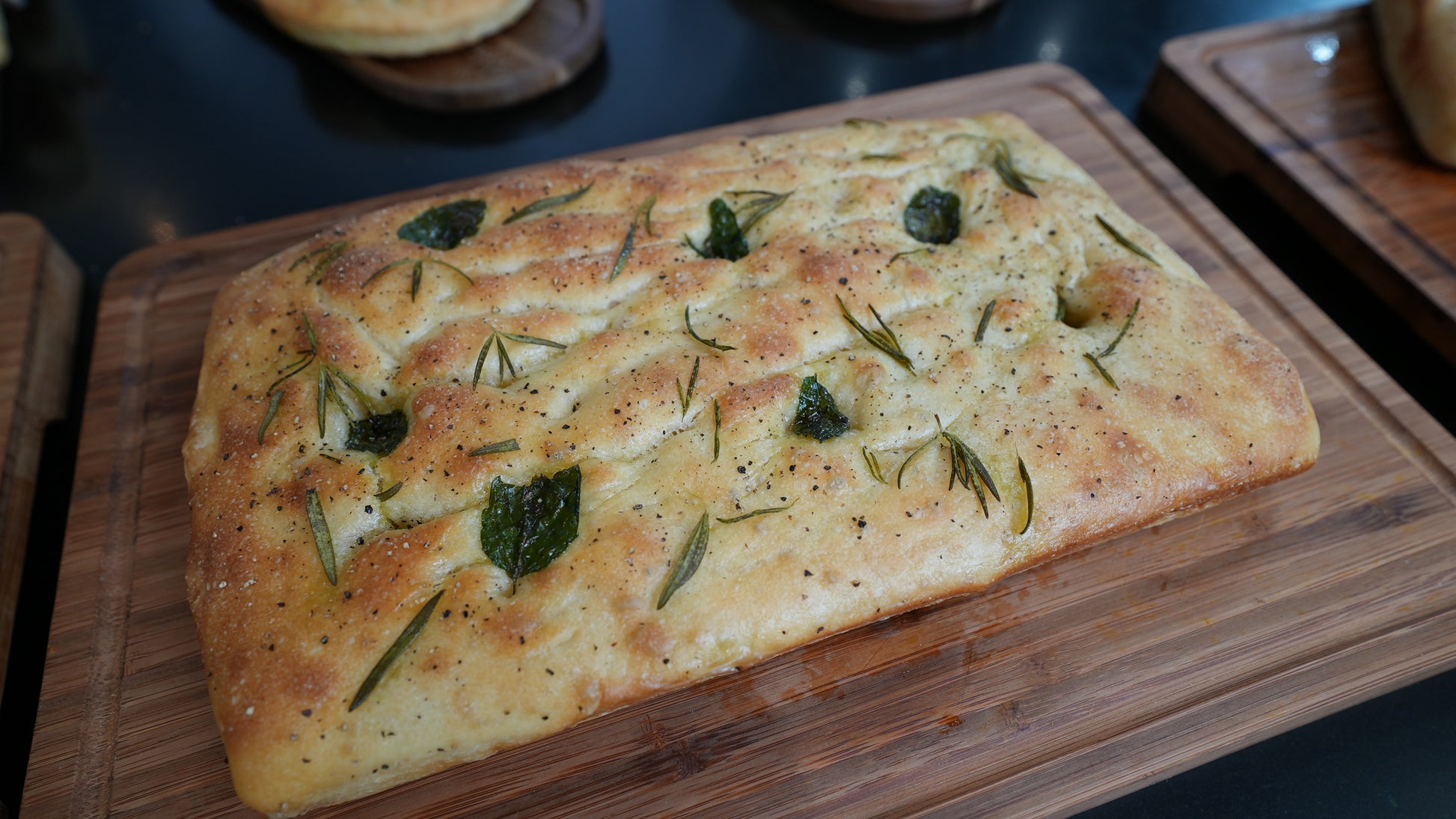 Gio Focaccia La Famiglia with herbs on a wooden cutting board