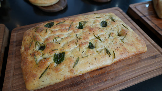 Gio Focaccia La Famiglia with herbs on a wooden cutting board