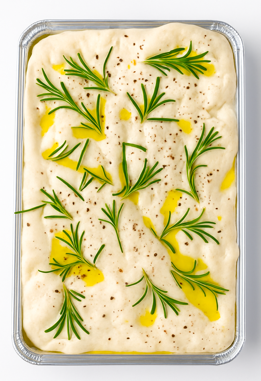 Unbaked focaccia bread with rosemary and olive oil in a baking tray.