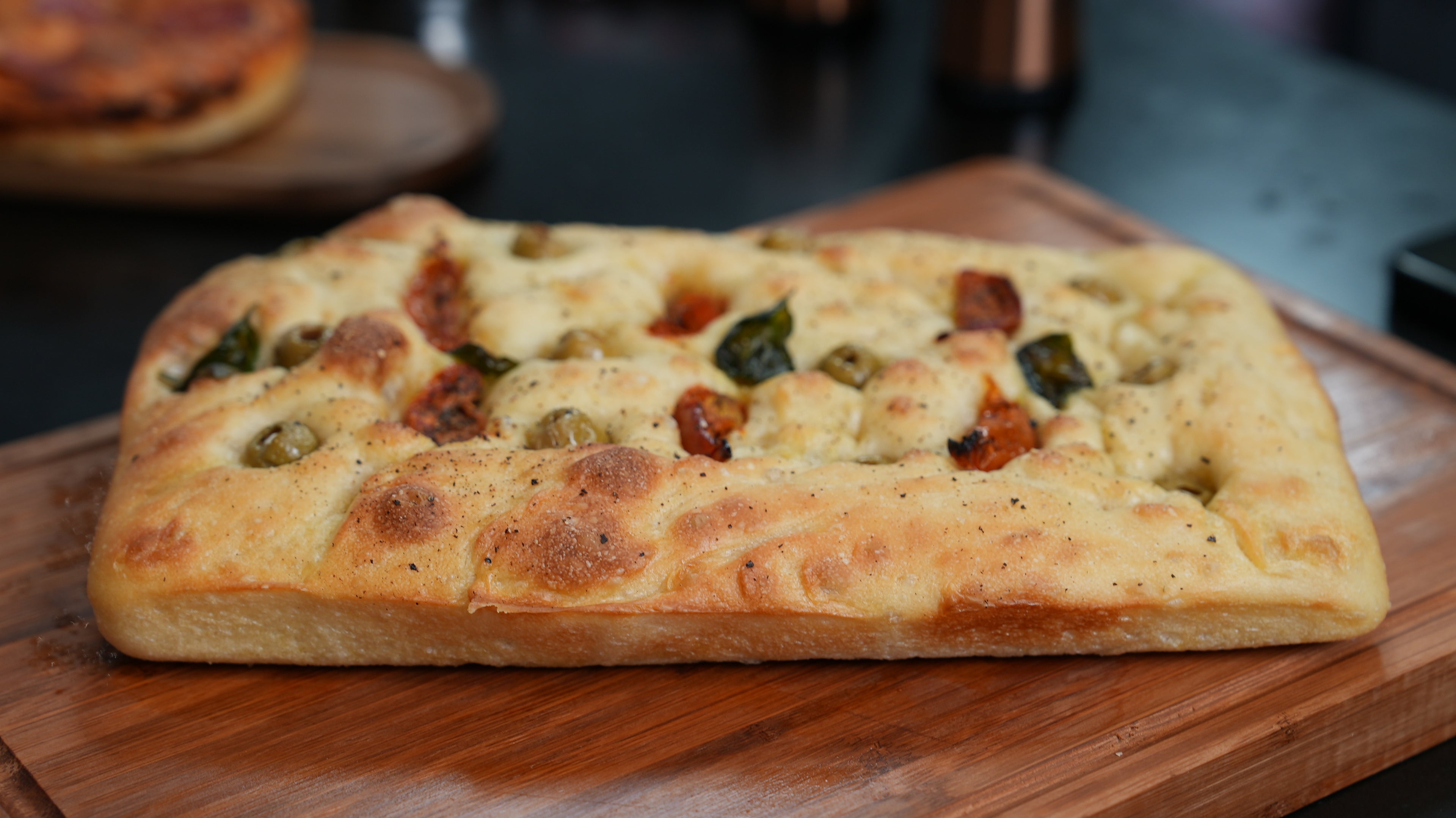 Large focaccia  with various toppings on a wooden board