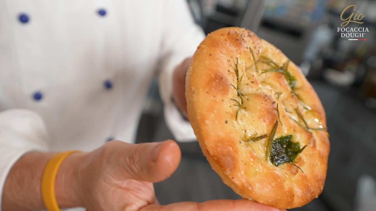 Gio holding a focaccia bread with herbs, blurred background