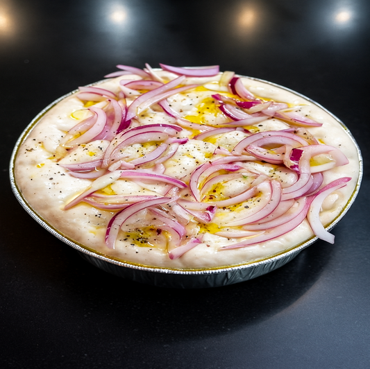 Uncooked focaccia with red onions on a dark background